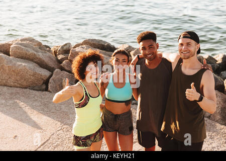Top view of four happy fitness people standing on pier near the sea and looking at the camera Stock Photo