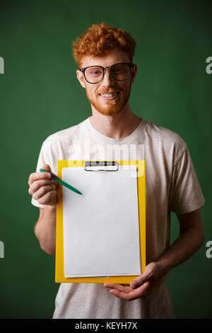 Smart readhead bearded man in white tshirt showing folder with copyspace, looking at camera, over green background Stock Photo