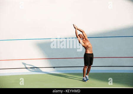 Full length portrait of a concentrated sportsman doing stretching exercises before workout on a track field outdoors Stock Photo