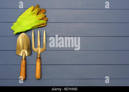 Gardening Hand Trowel, Hand Fork and pair of green work gloves on wooden blue boards Stock Photo