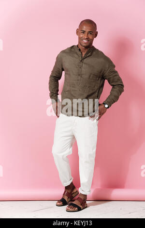 Full length image of smiling african man holding arms on hips and looking at the camera over pink background Stock Photo