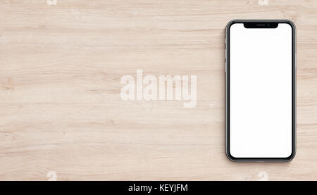 Smartphone similar to iPhone X mockup flat lay top view lying on wooden office desk. Banner with copy space. Stock Photo