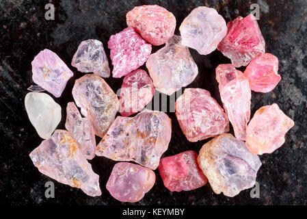 Collection of pink and red rough uncut spinel gemstones on black stone slate. Stock Photo