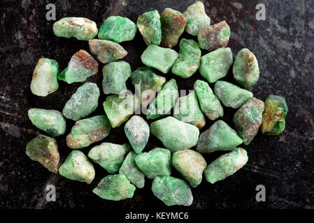 Collection of lovely green rough and uncut emerald gemstones on black stone slate. Stock Photo