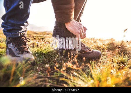 Active senior man on a walk in a beautiful autumn nature. Unrecognizable man tying his shoelaces. Close up. Stock Photo