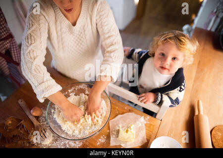 Unrecognizable woman and toddler boy making cookies at home. Mother and son baking gingerbread Christmas cookies. Stock Photo