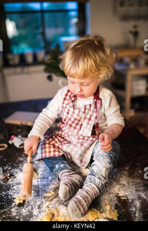 Toddler boy making gingerbread cookies at home. Little boy sitting on the table. Christmas time. Stock Photo