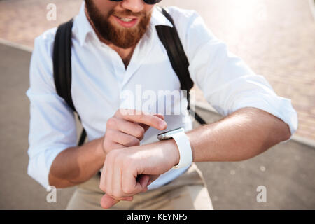 Cropped close up image of smiling bearded man using his wristwatch oudoors Stock Photo