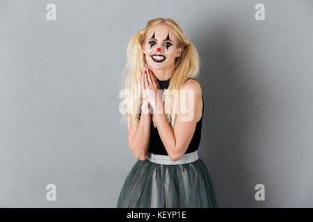 Portrait of a smiling blonde woman in halloween clown make-up posing while standing and looking at camera isolated over gray background Stock Photo