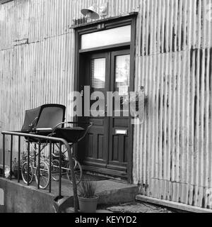 Old style vintage baby pram on front porch outside door of old house in black and white monochrome archival style square image, Reykjavik, Iceland Stock Photo