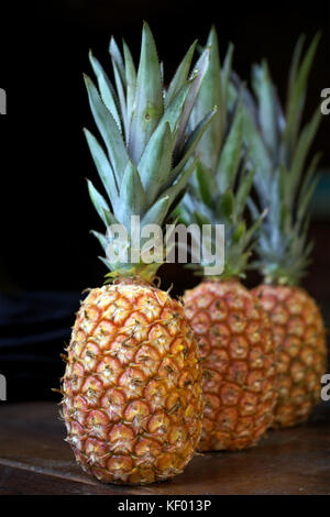 Close-up on three pineapples in a row on brown table and black background Stock Photo