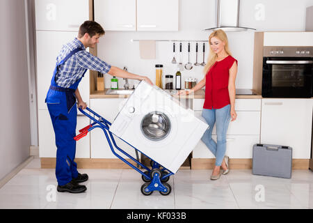 Young Happy Woman Looking At Male Worker Using Hand Truck For Carrying Washer In Kitchen Stock Photo