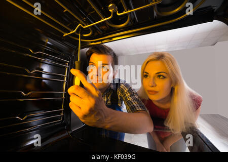 Young Woman Looking At Male Worker Repairing Inside The Oven Using Screw Driver Stock Photo