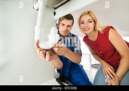 Male Plumber Showing Damage In Sink Pipe To Young Woman At Home Stock Photo