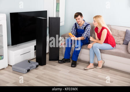 Technician Checking TV Speaker Sound System With Multimeter In Front Of Woman At Home Stock Photo