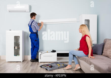 Male Carpenter Repairing Or Installing Furniture With Young Woman Sitting On Couch At Home Stock Photo