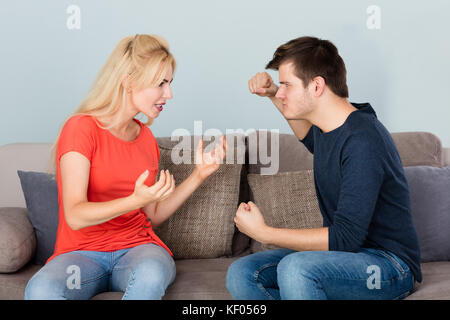 Young Frustrated Infidelity Couple Sitting On Couch Having Argument With Each Other At Home Stock Photo