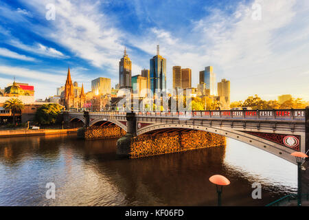 Warm bright sunlight lit Melbourne city over Princes bridge St Kilda road sun sunrise over waters of Yarra river. Stock Photo