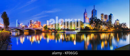 Blur colourful sunrise over Melbourne city CBD with bright downtown lights reflecting in still waters of Yarra and Prince bridge archs connecting Sout Stock Photo