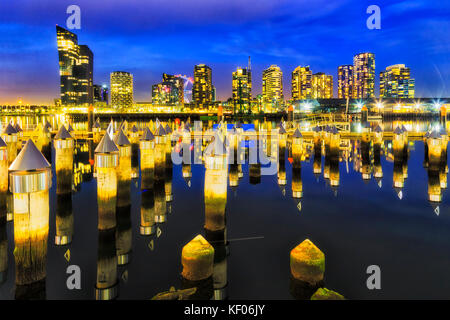 Matrix of timber jetty poles pinning out of still waters of Yarra river at Melbourne's docklands marina and suburb at sunset with bright reflecting il Stock Photo