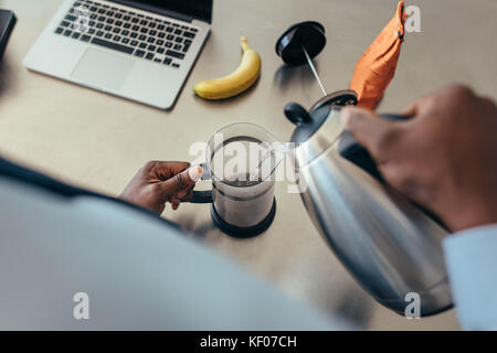 Man pouring hot water in coffee maker. Man preparing coffee on breakfast table with a laptop computer by the side. Stock Photo