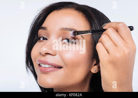 Close up of smiling woman applying eyeshadows Stock Photo