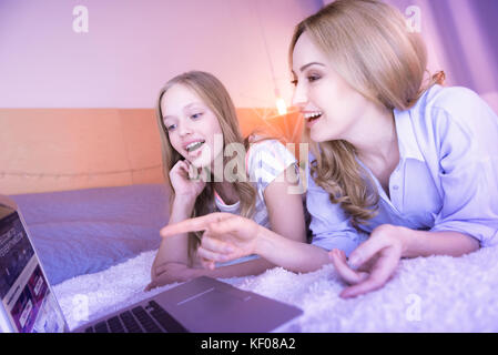 Smiling mom and daughter lying and using the laptop Stock Photo