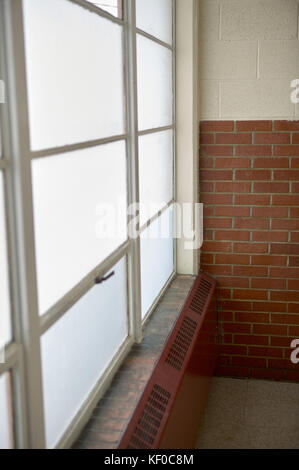 Old radiator under a metal framed window in a building with half face brick walls in a receding perspective view Stock Photo