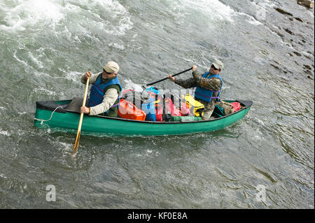 Two men navigate an overloaded canoe through rapids during an adventure on a wild Alaskan river. Stock Photo