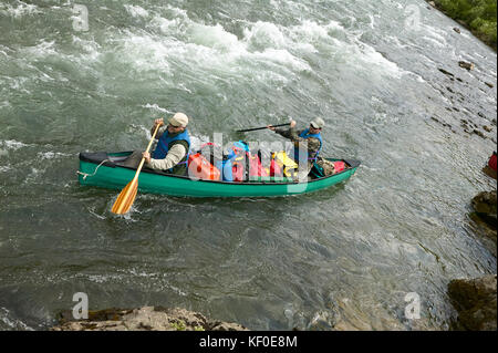 Two men navigate an overloaded canoe through rapids during an adventure on a wild Alaskan river. Stock Photo