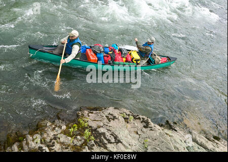 Two men navigate an overloaded canoe through rapids and rocks during an adventure on a wild Alaskan river. Stock Photo