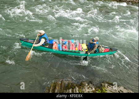 Two men navigate an overloaded canoe through rapids and rocks during an adventure on a wild Alaskan river. Stock Photo