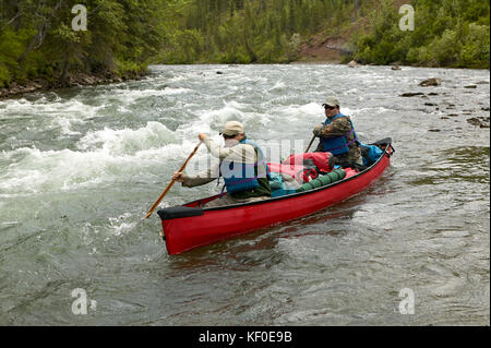 Two men navigate a canoe through rushing rapids during an adventure on a wild Alaskan river. Stock Photo