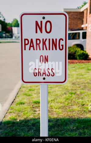 A close up of a red and white no parking on grass sign on a residential street. Stock Photo