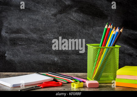 School supplies on wooden table and blackboard background. Back to school concept. Copyspace. Stock Photo