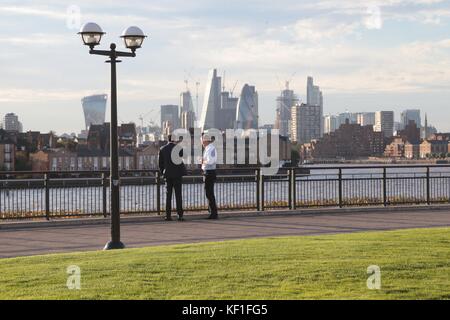 Workers relax during their tea and coffee breaks in the autumn sun at Canary Wharf over looking The River Thames and The City of London. Stock Photo