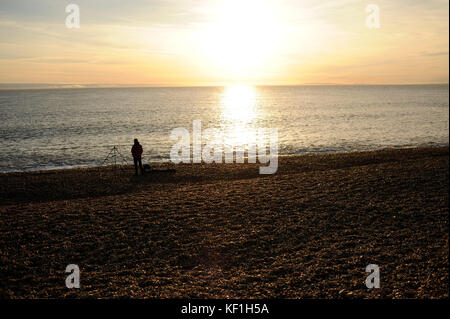 Keyhaven, UK. 25th October, 2017. A man fishes in the waters off Hurst Spit, Keyhaven, Hampshire as the sun sets on the horizon. A fiery sunset over the south coast ended a warm and sunny autumn day in southern England. Credit: David Cliff/Alamy Live News Stock Photo