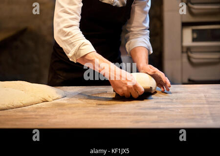 baker portioning dough with bench cutter at bakery Stock Photo