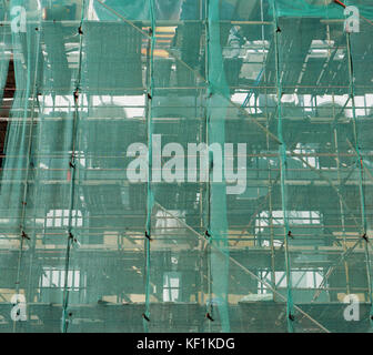Green plastic mesh on the wall of a renovated urban building protects people from stones. Outdoor industrial background Stock Photo