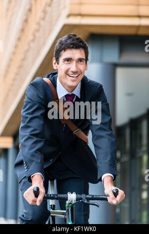 Active young man smiling while riding utility bicycle to his wor Stock Photo