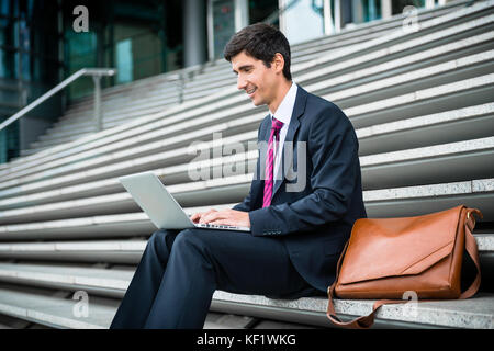Young businessman using a laptop while sitting down outdoors  Stock Photo