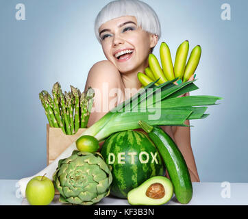 Happy young girl with an abundance of fruits and vegetables. Photo of smiling blonde girl on blue background. Healthy lifestyle concept Stock Photo