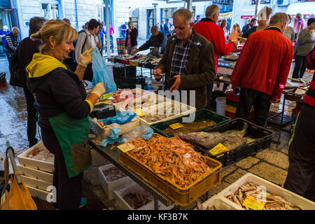 A customer hands over paper notes to a woman who's bagged up his order of freshly caught fish in Split's bustling fish market one autumn morning. Stock Photo