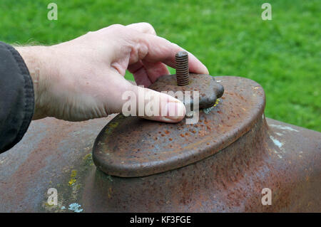 The hand of the elderly farmer unscrews the lid on the water radiator of an old rusty retro tractor. Autumn day outdoor concept shot. Soft focus Stock Photo