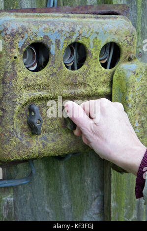 The hand of an elderly woman switches electricity on an old rusty retro rural switchboard. Concept outdoor autumn day photo Stock Photo