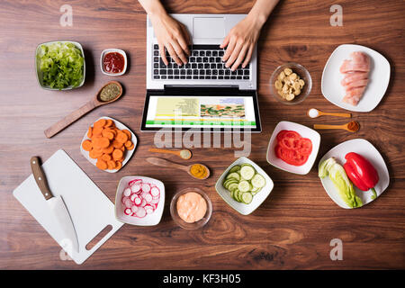 High Angle View Of Woman Looking At Recipe On Laptop While Cooking In Kitchen Stock Photo