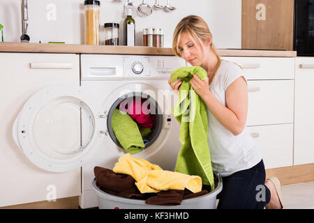 Young Woman Smelling Cleaned Clothes After Washing Near Washing Machine Stock Photo