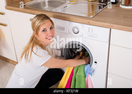 Young Woman Looking At Clean Clothes Out Of Washing Machine In Kitchen  Stock Photo - Alamy