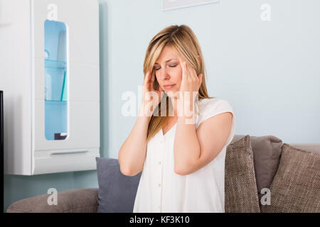 Young Woman Suffering From Headache While Sitting On Sofa At Home Stock Photo
