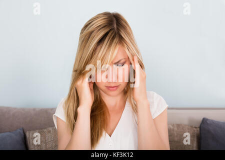 Young Woman Suffering From Headache While Sitting On Sofa At Home Stock Photo